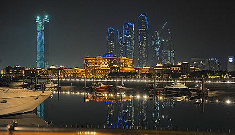 Abu Dhabi skyline at night showing Emirates Palace and Etihad Towers in the background.